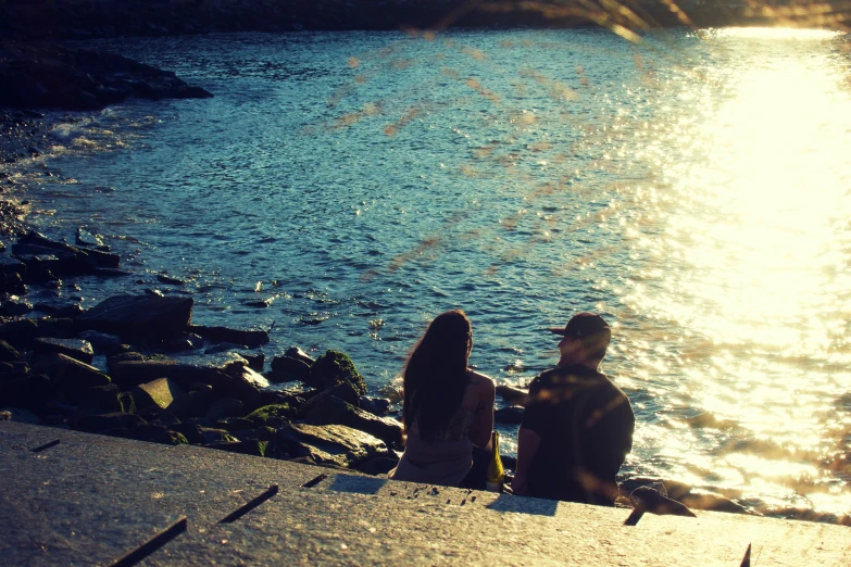 a man and woman sitting by the water with bright sun shining
