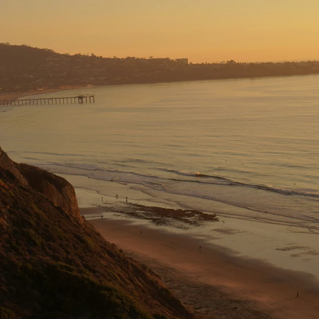 a beach is shown with a wooden pier in the distance