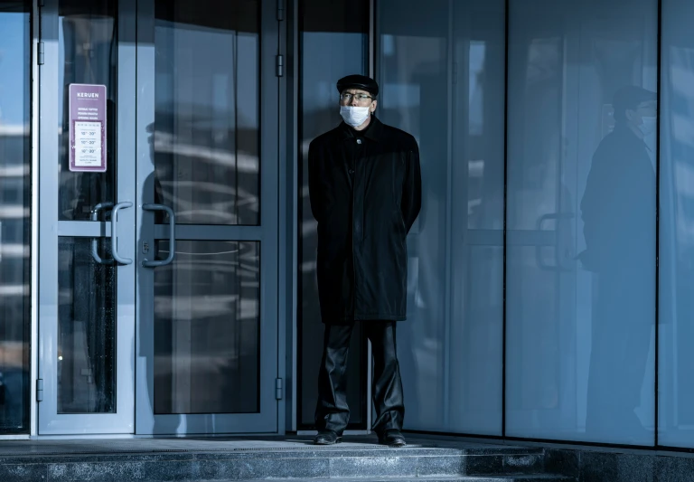 a man wearing a face mask standing in front of glass doors