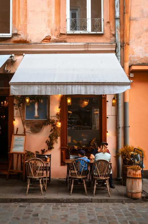 two people sitting outside of a restaurant with a white awning