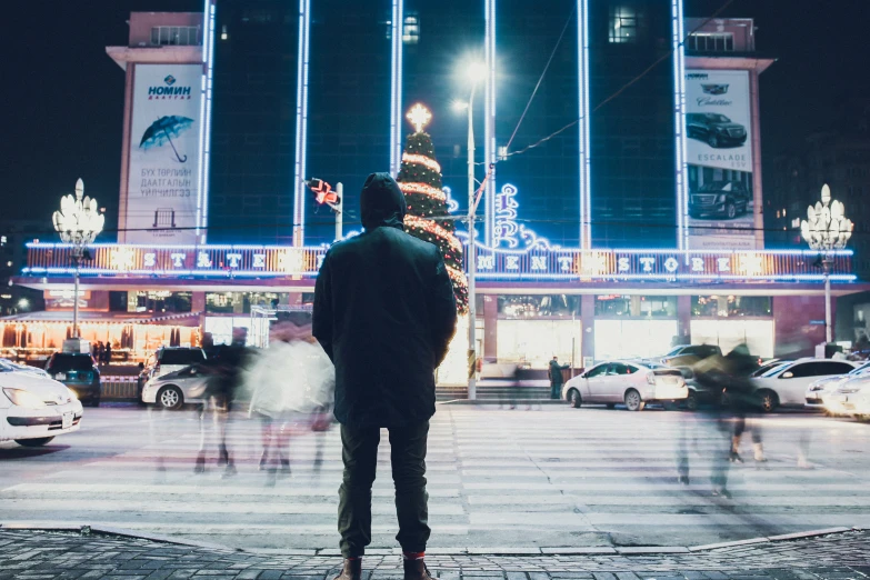 person standing on the side of a street in front of a building with christmas lights