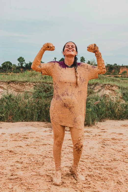 a woman covered in mud with hands raised above her head