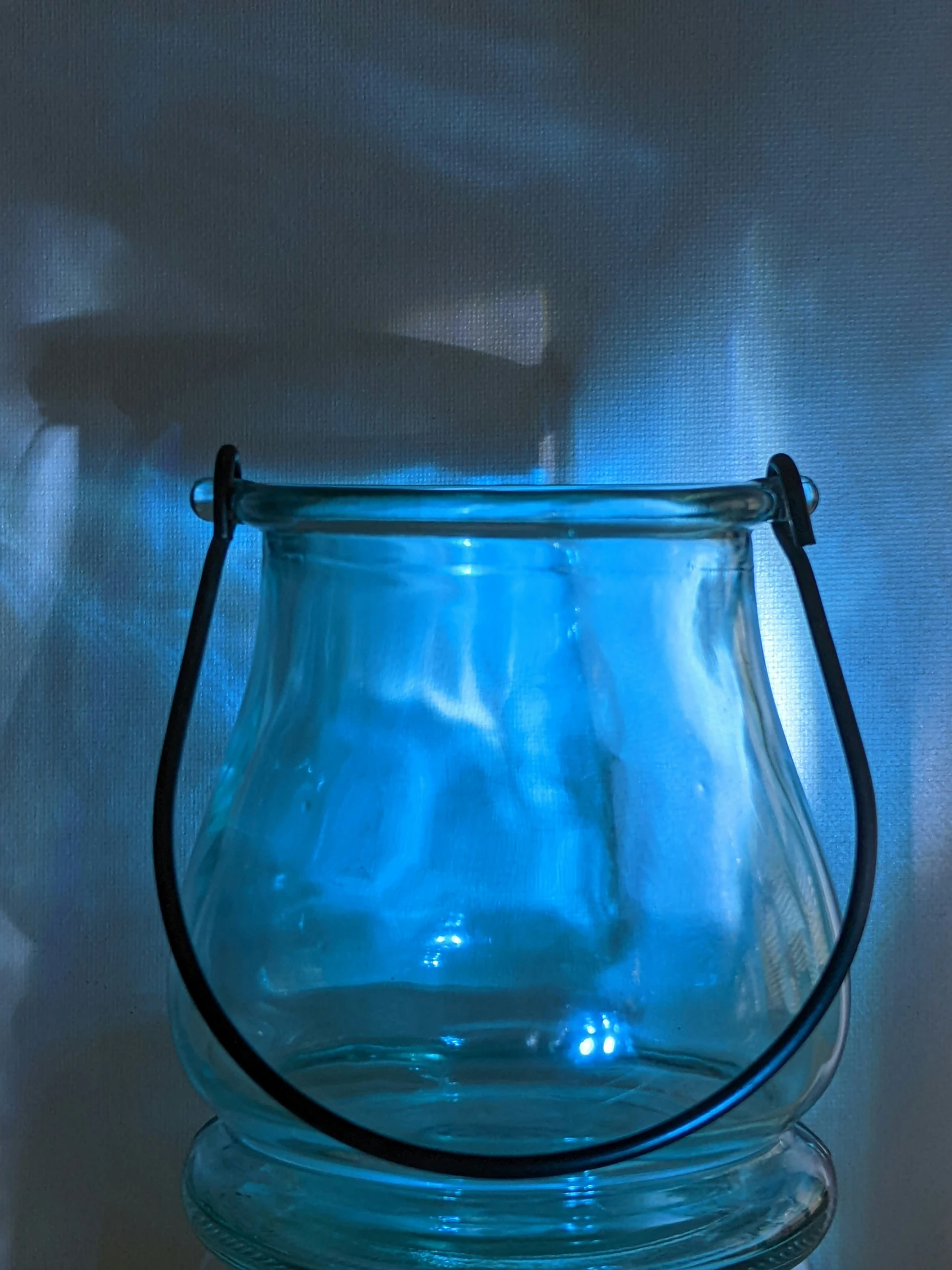 blue glass vase with black handles on a white surface