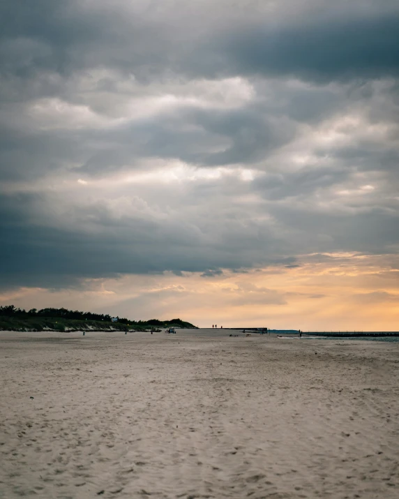 a cloudy day at the beach with people walking in the sand