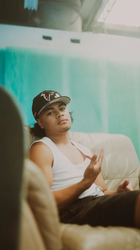 a man wearing a cap talking to someone sitting on a couch