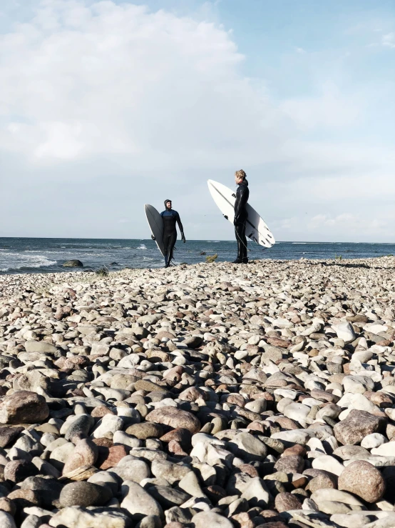 two people standing on a beach with their surfboards in hand