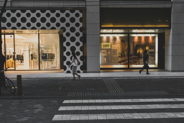 a woman walking across a cross walk past a building