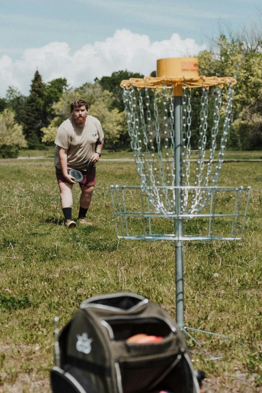 a man holding a frisbee in front of a metal disc golf basket