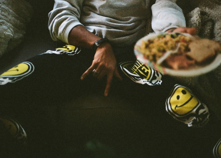 a person sitting on a couch holding a plate with a bowl of food
