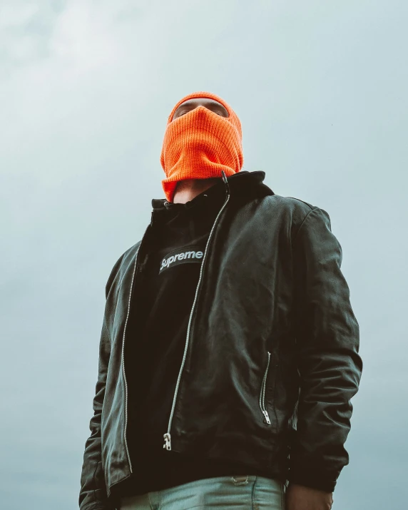 man wearing orange knit mask with sky in the background