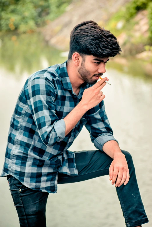 a man sitting on the bank of a river and holding his hands to his mouth