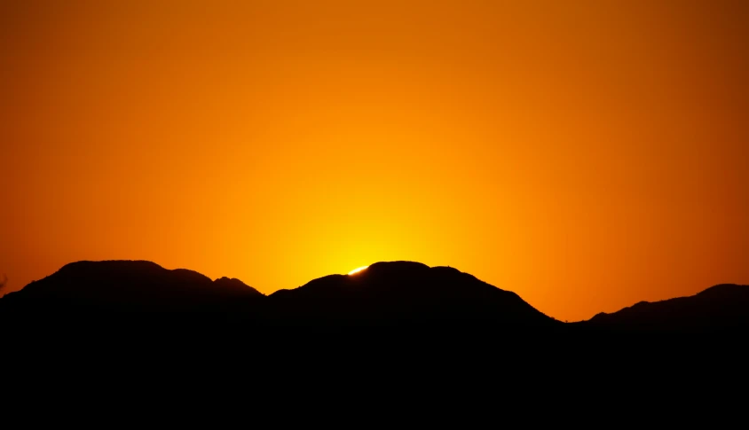 the sun setting behind some mountains on the horizon