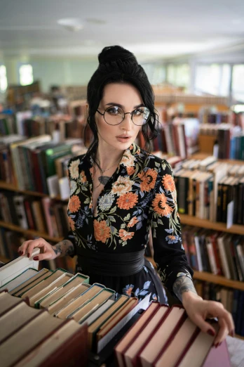 a woman wearing glasses leaning on a shelf full of books