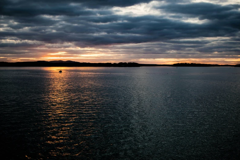 a boat sitting on top of a lake under cloudy skies