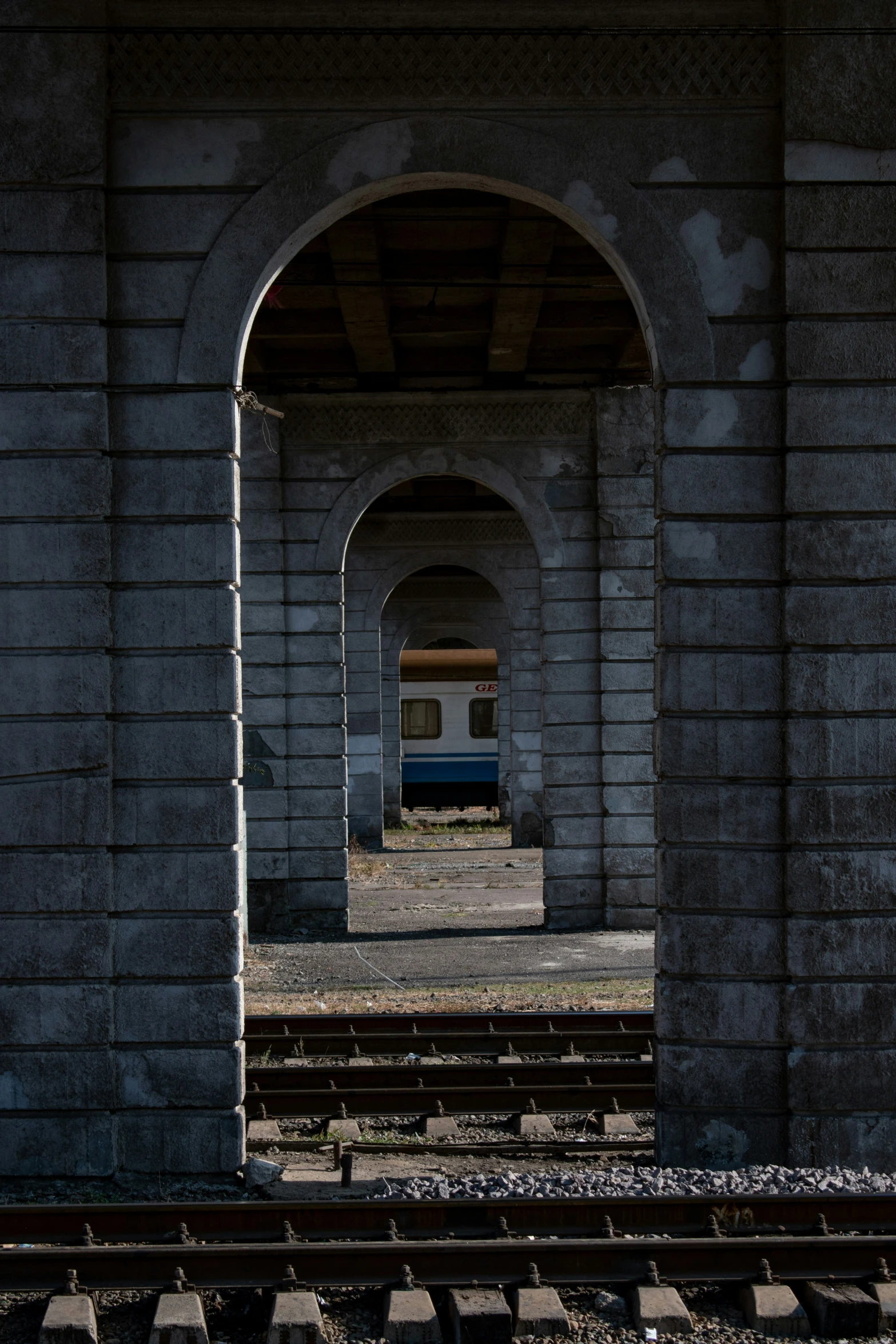 there is a blue train traveling underneath an arch