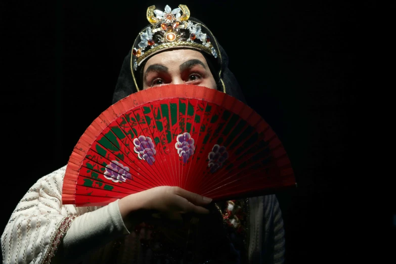 a woman with a veil and headpiece holding an orange fan