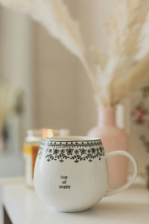 a white cup with flower design on the side sits on a shelf