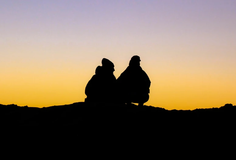 the two people are sitting at dusk on the hill