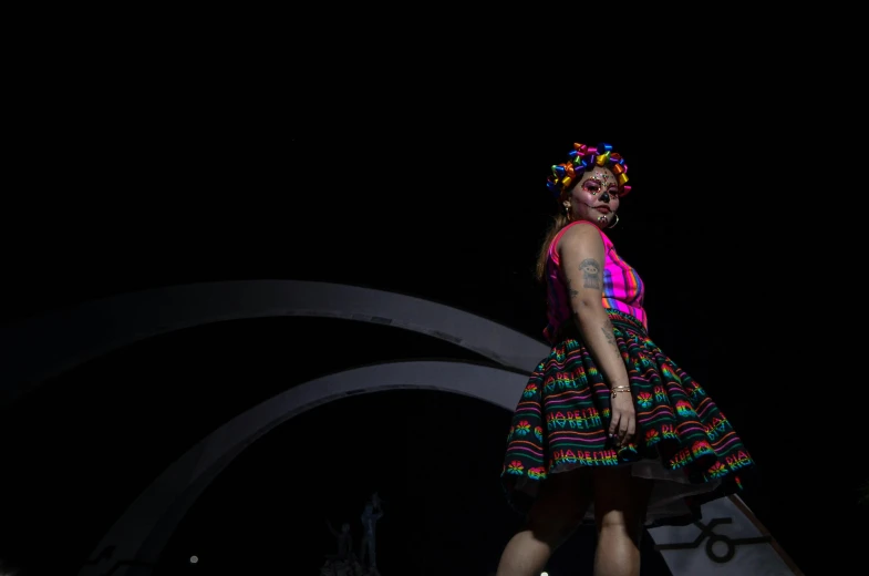 a woman standing alone on a catwalk on a dark background