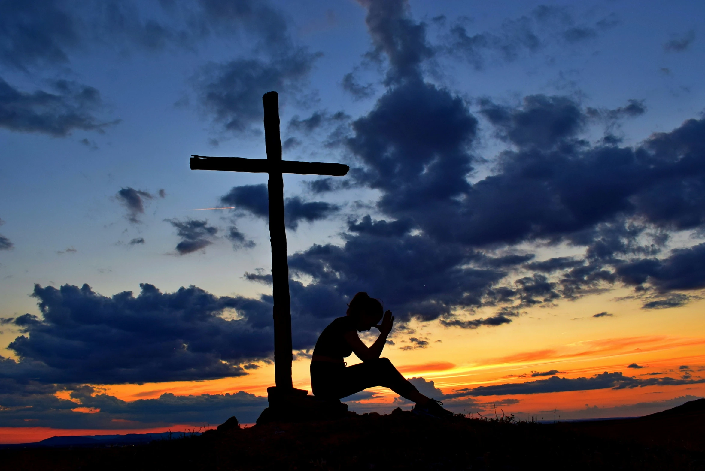 the silhouette of a man sitting in front of a cross