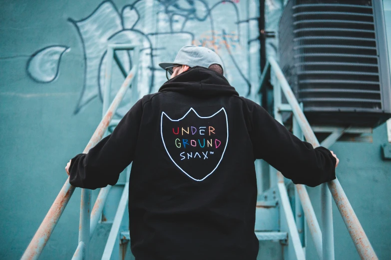 a man wearing an unisex hoodie walks down stairs in front of graffiti on the side of a wall