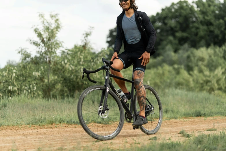 a man with tattoos on his knees and leg in black biker outfit riding a bike in the woods