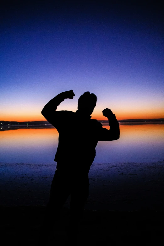 a silhouette image of a man with his arms outstretched and a body of water behind him