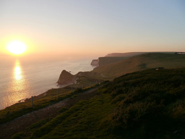 the sun setting over an ocean with two steep hills