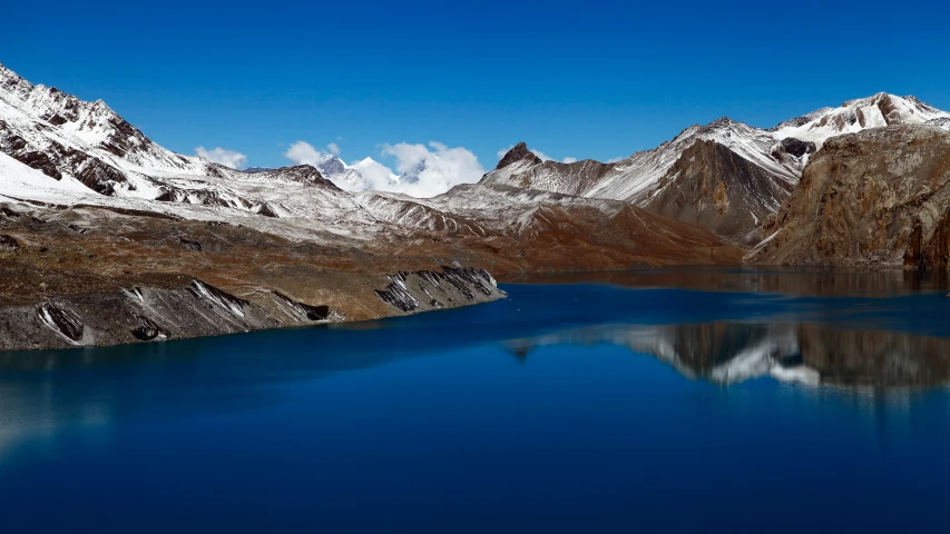 snow - capped mountains are shown next to a still blue lake