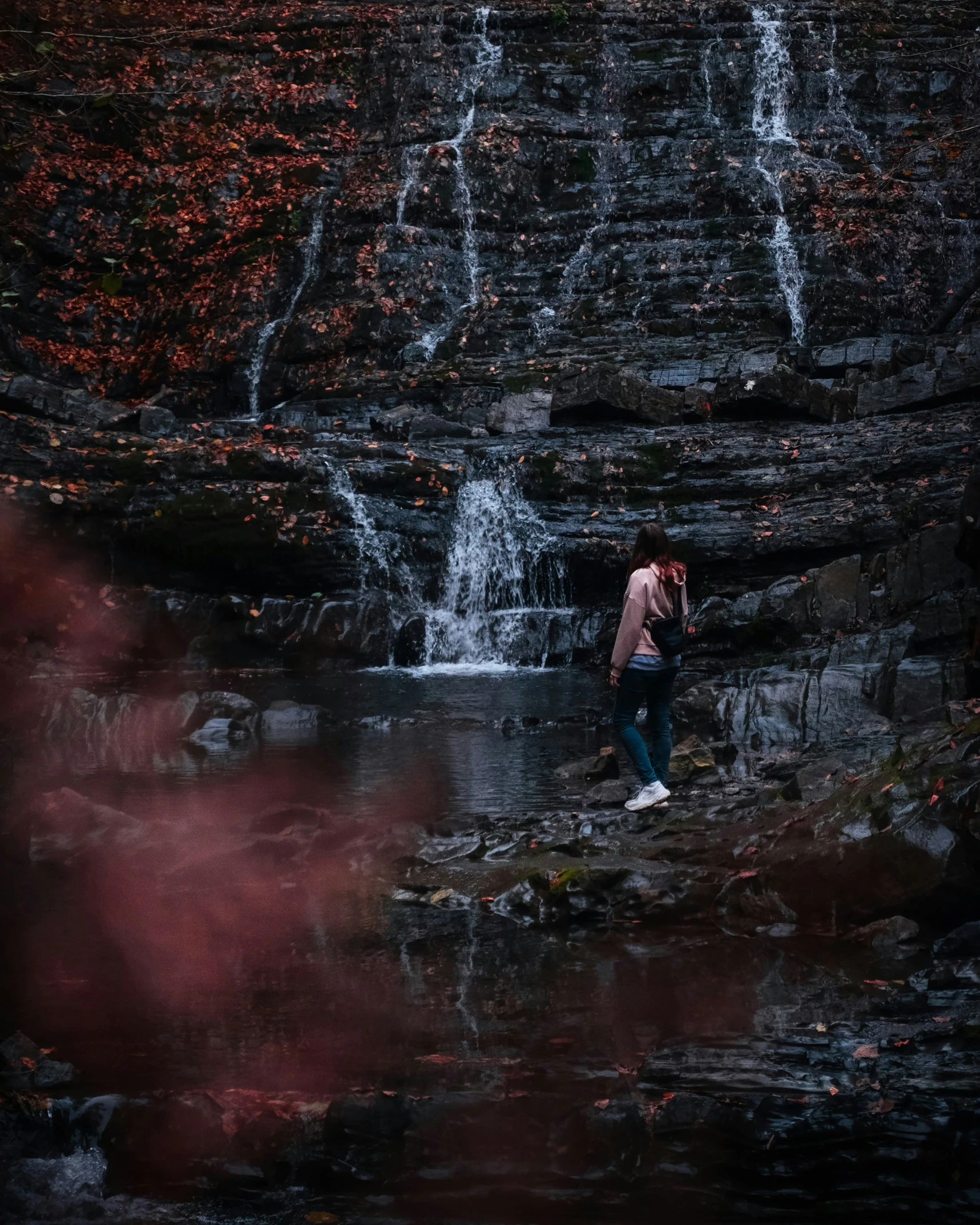 two people standing under a waterfall in the woods