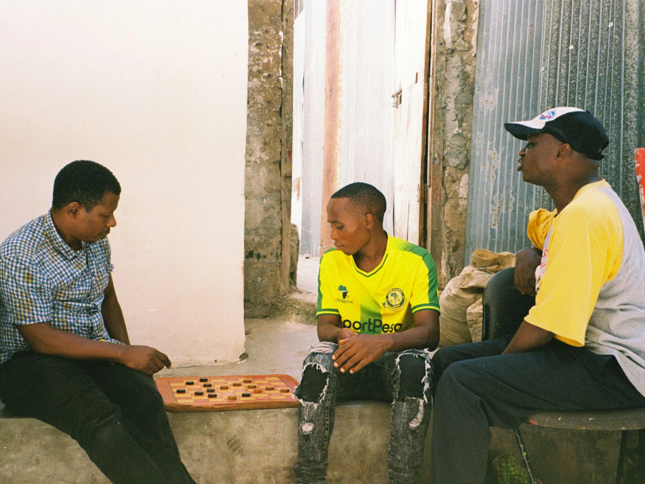 three men sit on benches playing board games