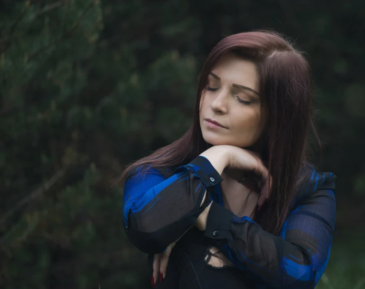 a woman wearing an elegant blue and black dress and black gloves is staring away while sitting outdoors