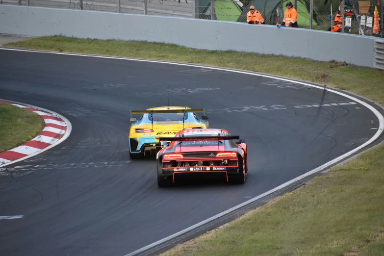 two racing cars on a race track, one with orange wheels