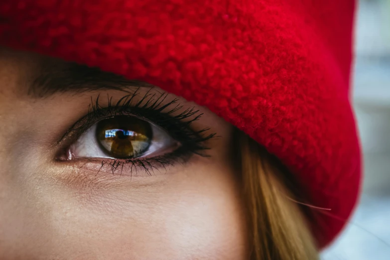 a close - up of a woman with big eyelashes and brown eyes wearing a red hat