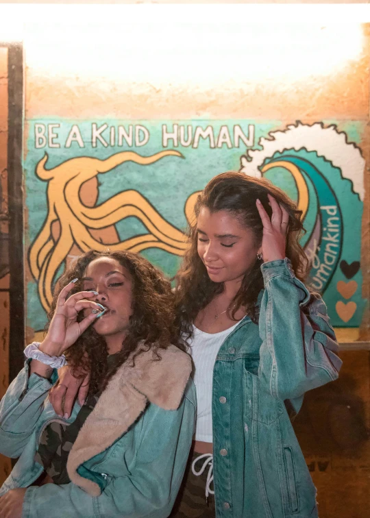 two young women standing in front of a sign talking on their phones