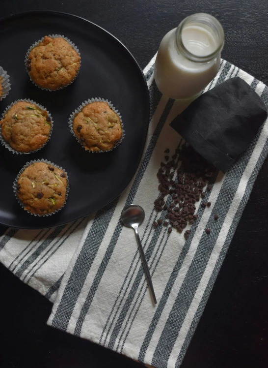 a black plate topped with muffins next to a glass of milk