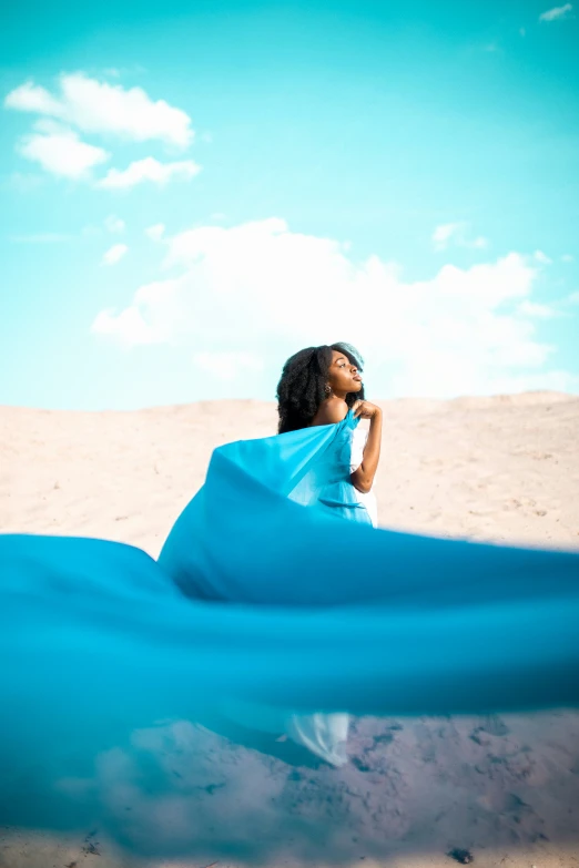 an african american woman wrapped in blue cloth sits on the beach