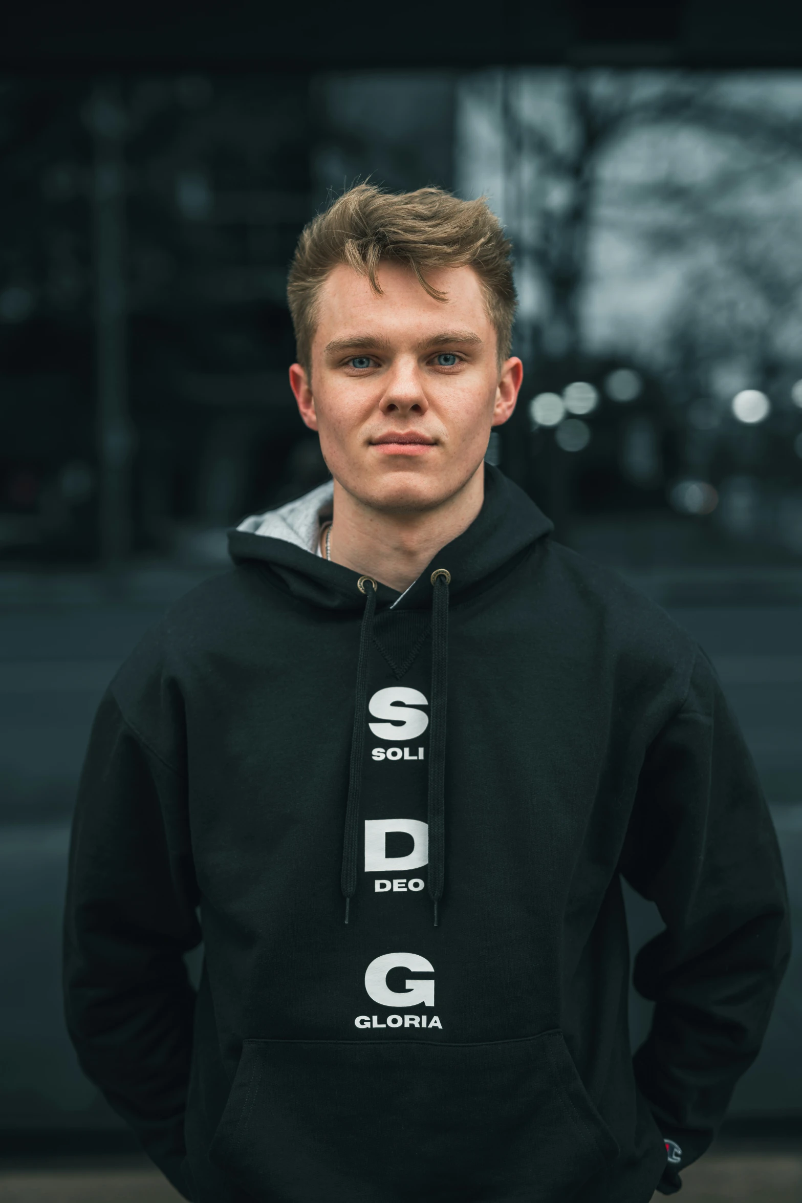 a young man in a black pullover and jeans stands against a wall