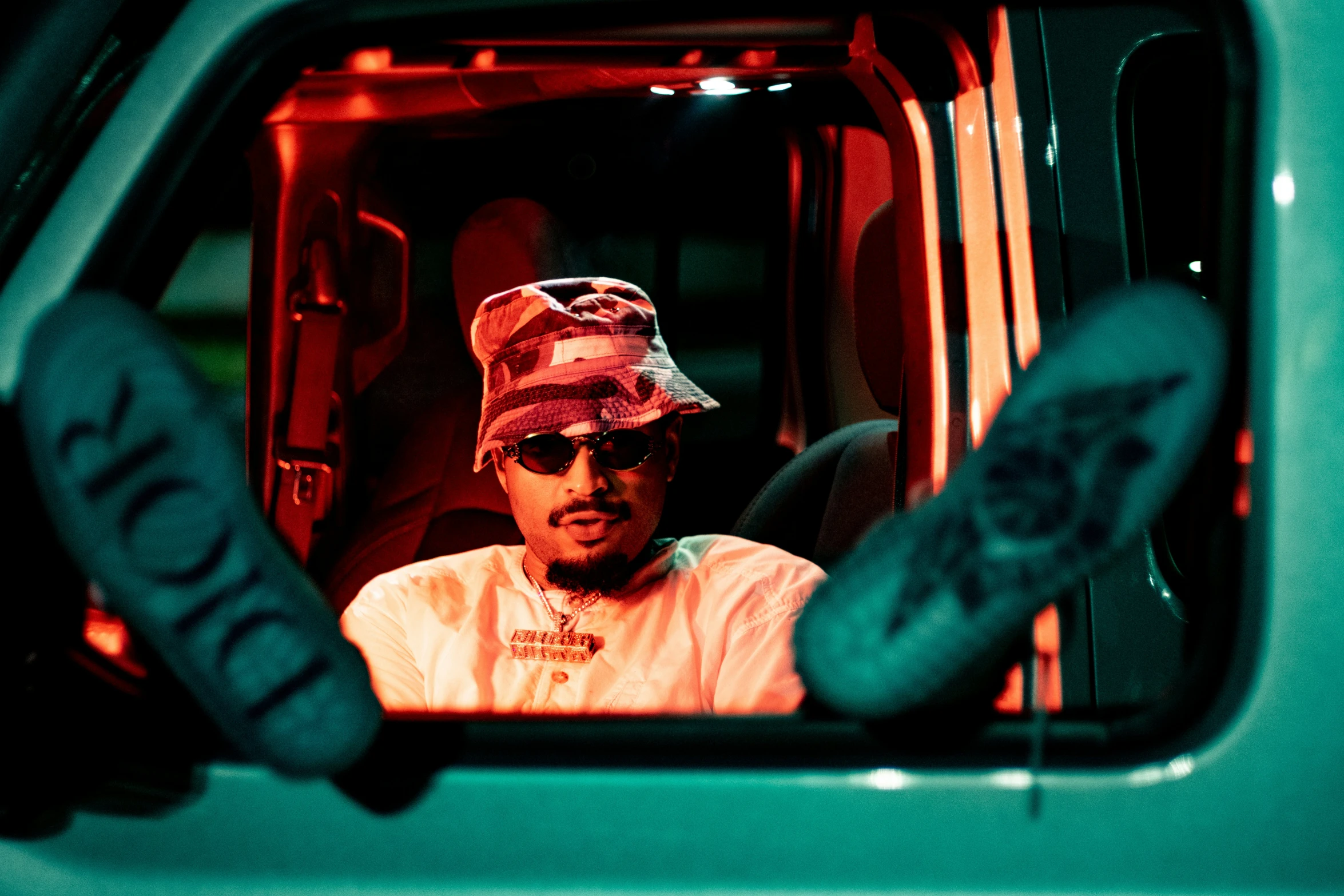 the reflection in the side view mirror shows a man with hat and sunglasses