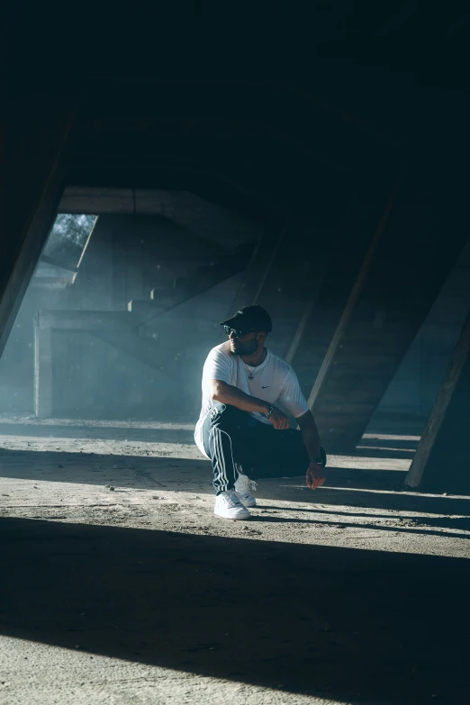 a person squats in the dirt under a bridge