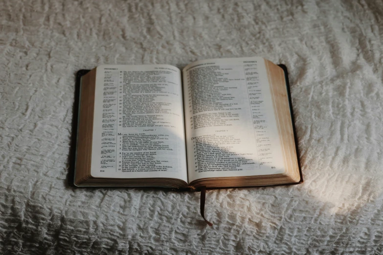 an open bible on a bed covered with linens