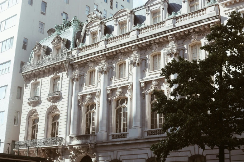 an ornate building stands in the sun behind many trees