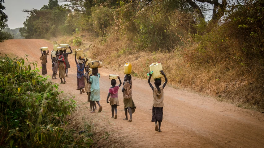 children carry heavy items on their heads as they head down the road