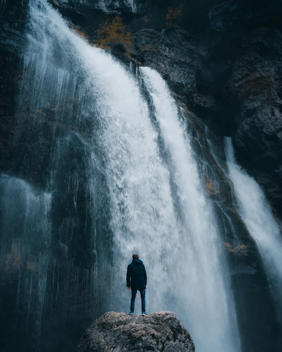 there is a man standing at the base of a large waterfall