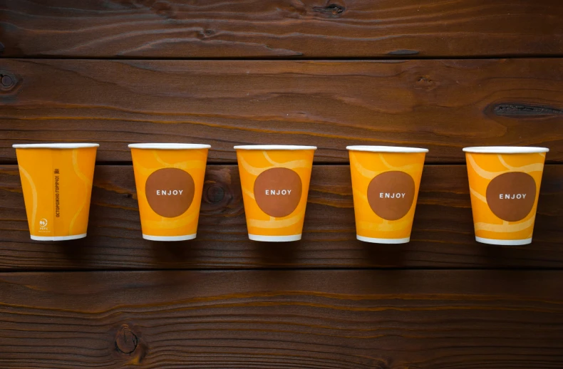 six paper cups with brown labels in front of a wooden table