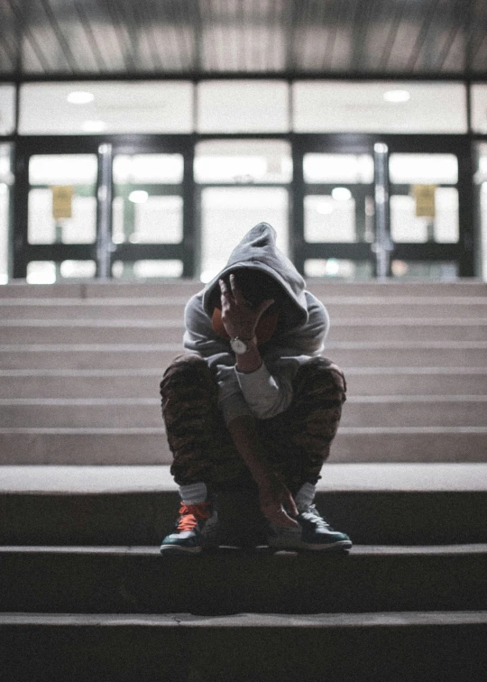 the young person sits on a step while listening to a cell phone