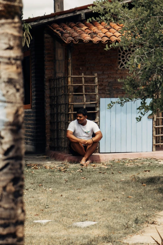 a man sits in front of his shack on a lawn