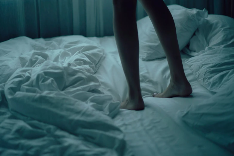 barefoot person walking on a bed surrounded by covers