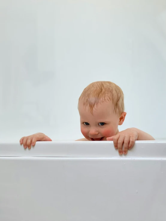 a baby is peeking over the edge of a bathtub