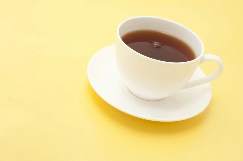 a white cup of tea sitting on top of a yellow table